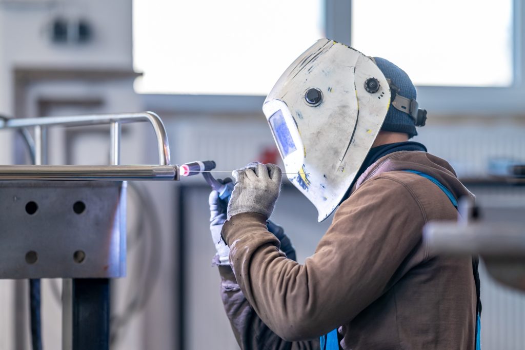 A man in a welding helmet is using gas to weld metal in a factory