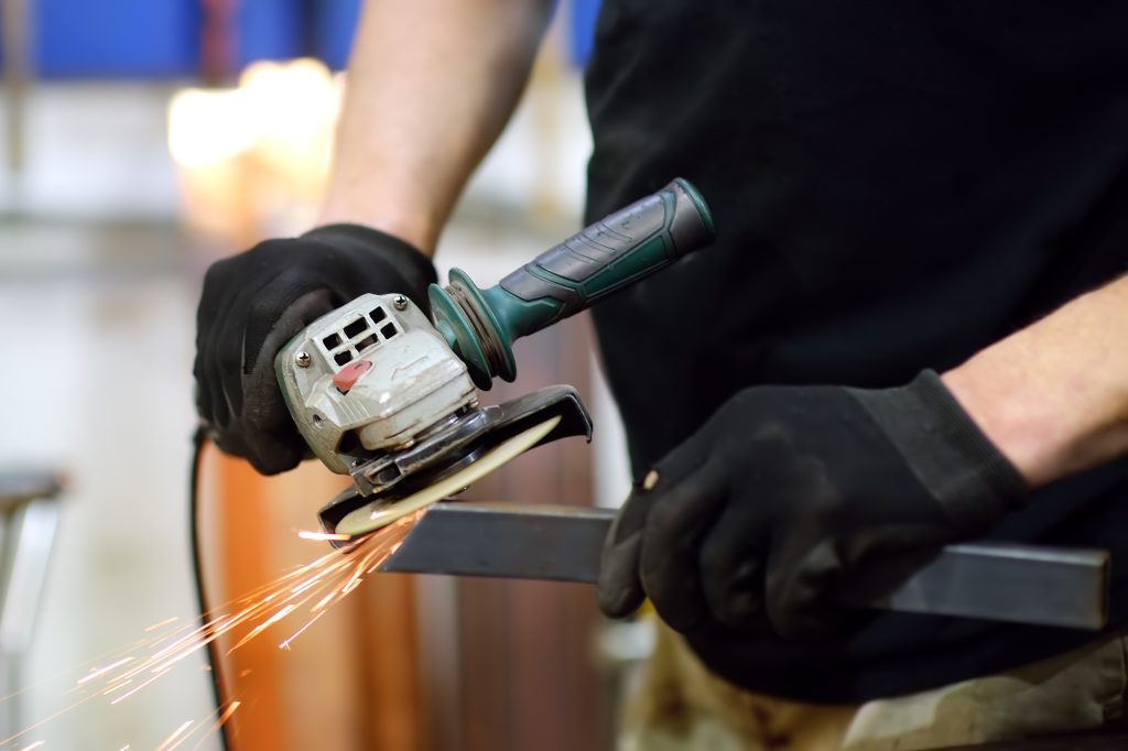 Metalwork craftsman cutting metal with grinder tools.