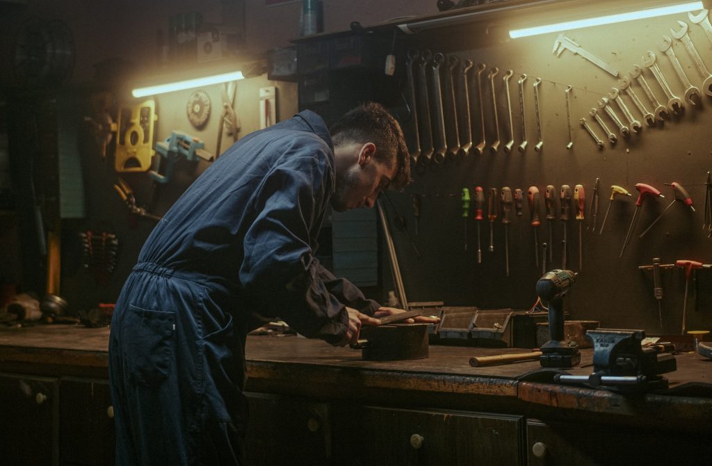 Male person in awesome workshop background he sanding a piece of iron or steel in his workshop
